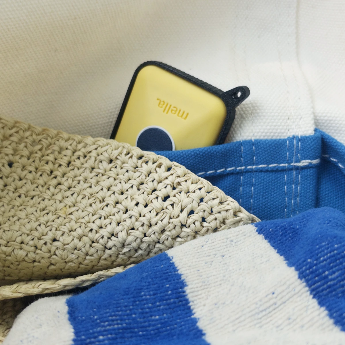 A citrus-yellow Mella prototype tucked inside a woven beach bag with a blue and white striped lining.